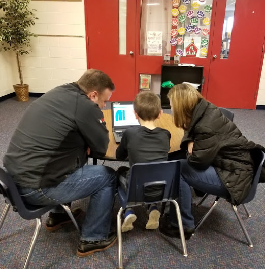 Parents learning huddled around a laptop with their child, learning how to code during Hour of Code week